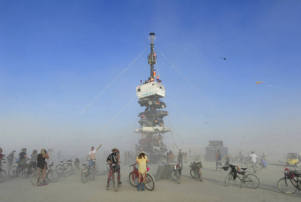 Burners are surrounded by playa dust climb onto an art installation titled, "Night of the Climb ...