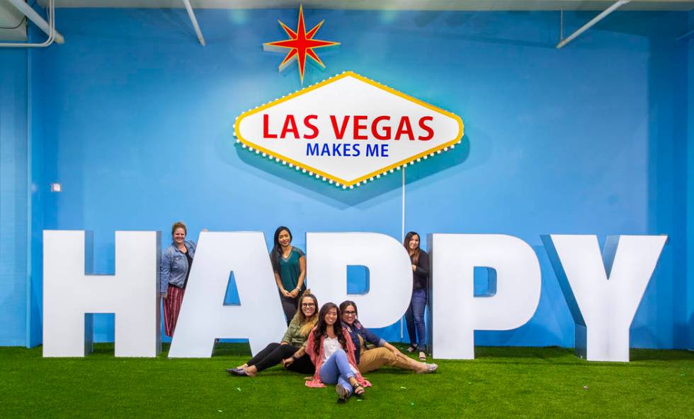 Friends strike poses about the signs in the Happy Room at the new Happy Place popup at Mandalay ...