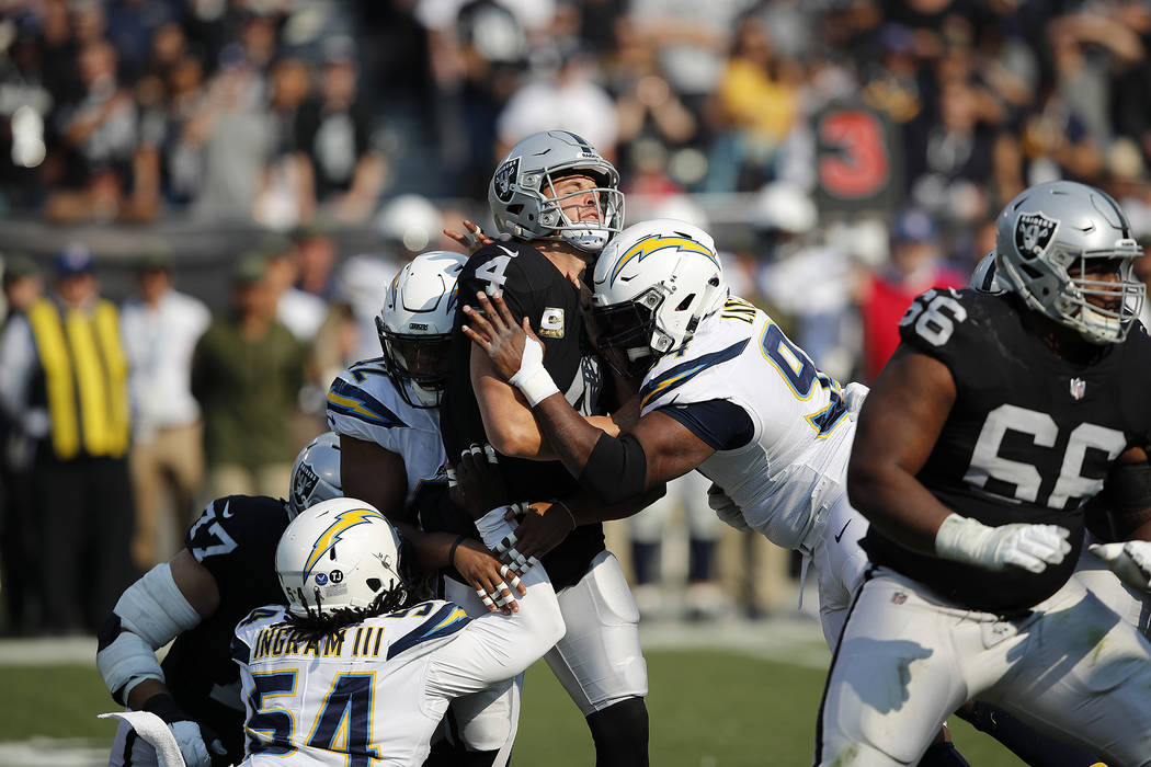 Oakland Raiders quarterback Derek Carr (4) is hit between Los Angeles Chargers linebacker Uchen ...