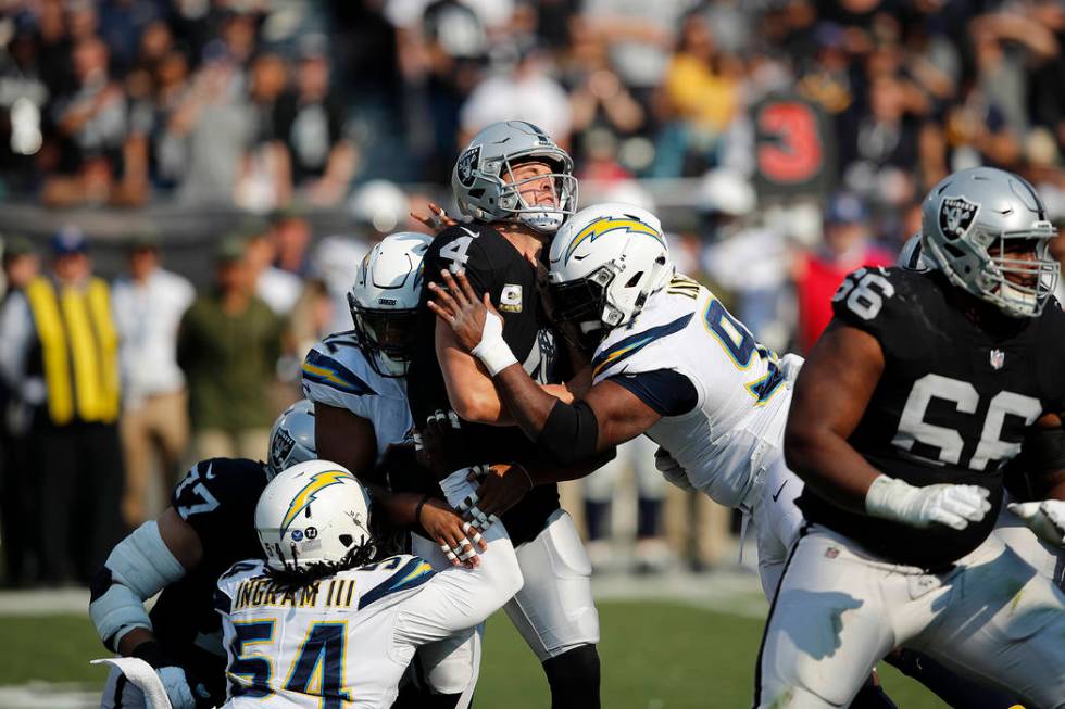 Oakland Raiders quarterback Derek Carr (4) is hit between Los Angeles Chargers linebacker Uchen ...