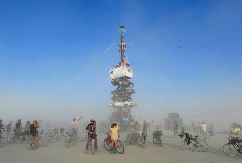 "Burners" surrounded by playa dust climb onto an art installation titled "Night of the Climb" a ...