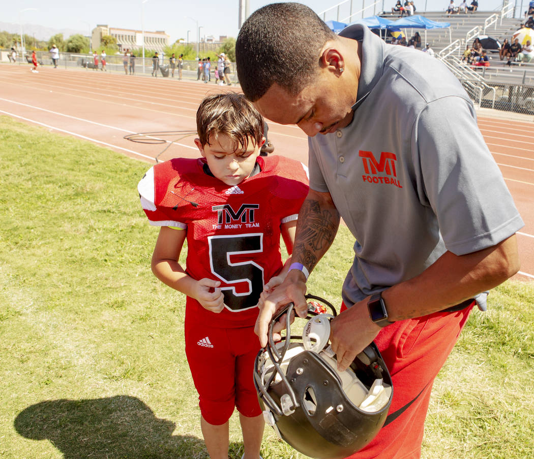 Devin Conway, right, fixes the helmet of TMT Red Lions player Noah Hamly, 8, during a youth foo ...