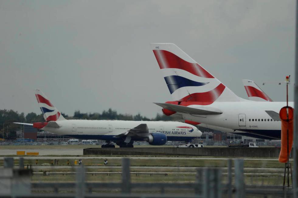 A British Airways plane, at left, is towed past other planes sitting parked at Heathrow Airport ...