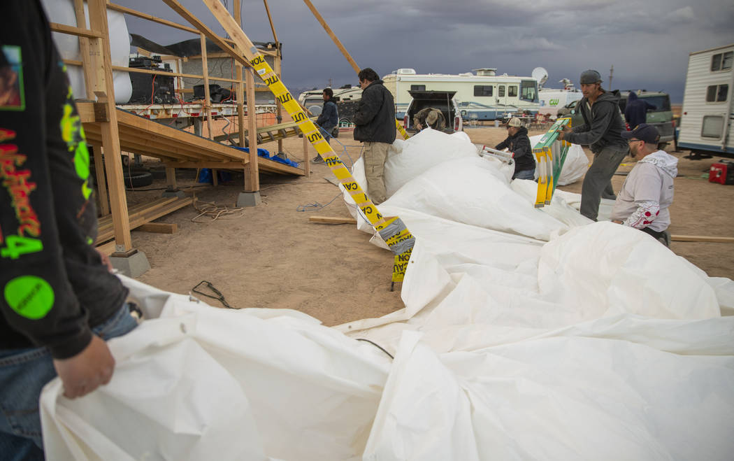 Volunteers help to secure the roof tarp from the main stage after it blows off from increasing ...