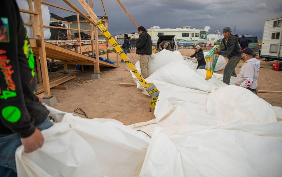 Volunteers help to secure the roof tarp from the main stage after it blows off from increasing ...