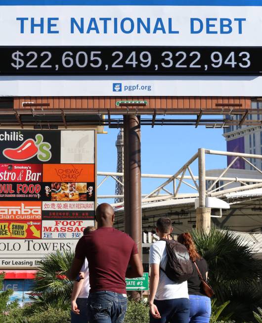 Pedestrians walk past a billboard depicting rising national debt on Las Vegas Boulevard directl ...