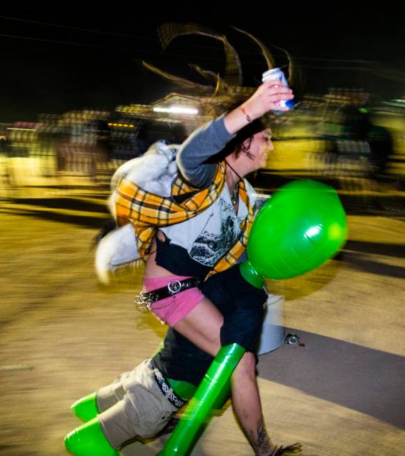 A festivalgoer rides an alien while drinking a beer in the mosh pit at the punk rock stage duri ...