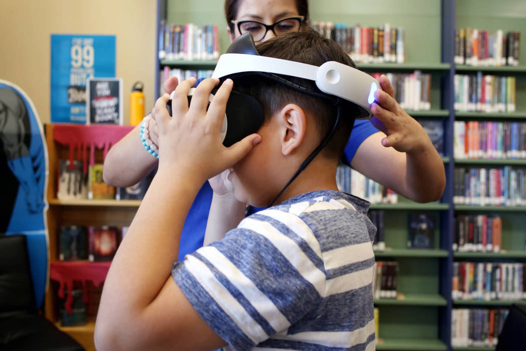 Senior youth service specialist Andrea Daciuk, Las Vegas, helps puts on VR goggles on Dominic G ...