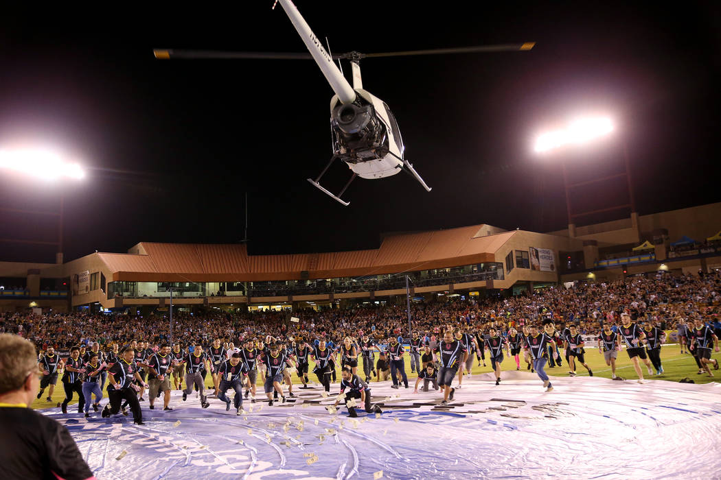 Fans rush to collect $5,000 dropped from a helicopter at half time during an USL soccer game be ...
