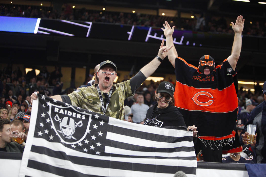 Oakland Raiders fans hold up a flag as a Chicago Bears fan cheers during an NFL game between th ...