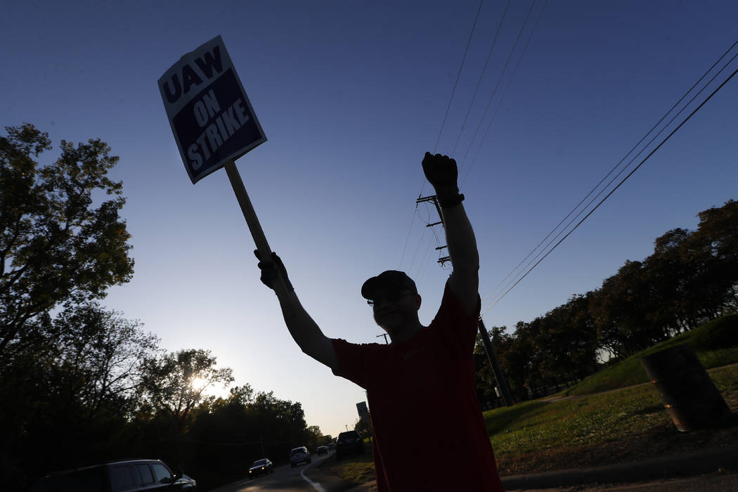 A member of the United Auto Workers cheers on honking cars as he walks the picket line at the G ...
