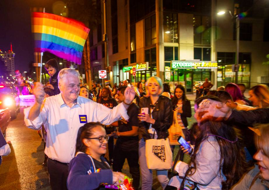 Governor Steve Sisolak waves a flag and helps to pass out Skittles while marching in the Pride ...