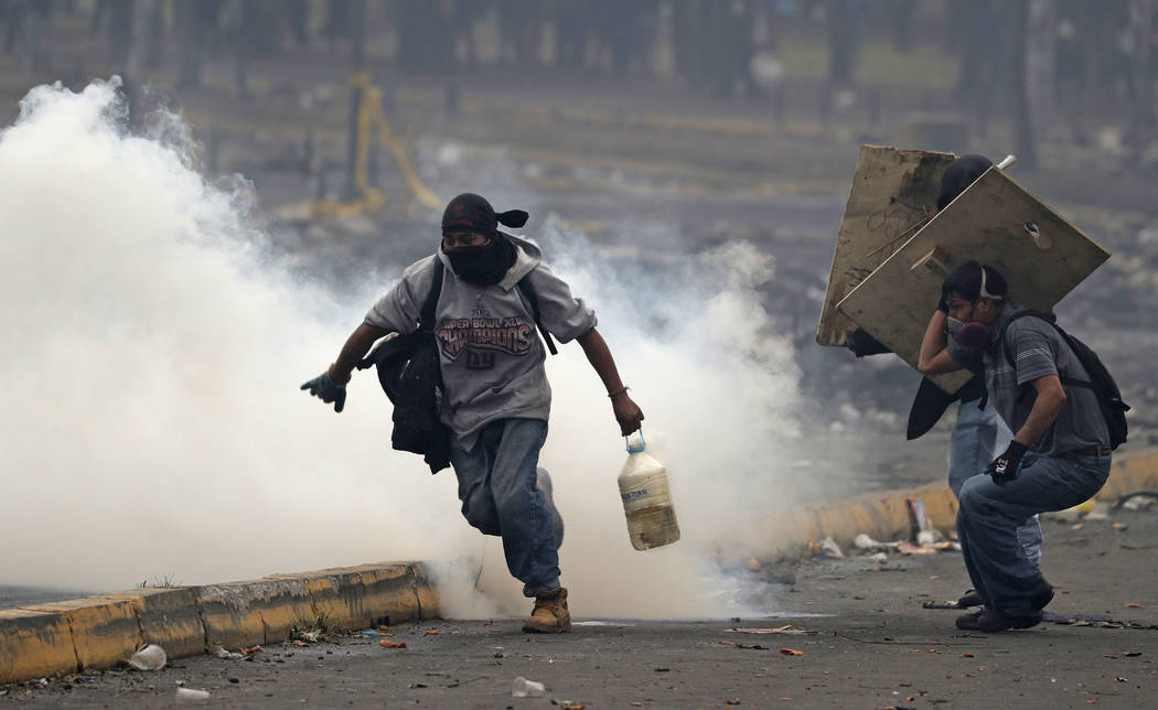 An anti-government protester carries a container of water, with an active tear gas canister ins ...