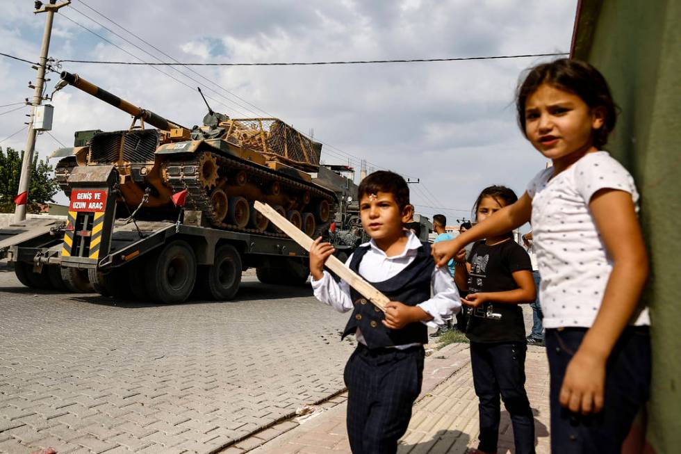 Children watch as army tanks are transported on trucks in the outskirts of the town of Akcakale ...