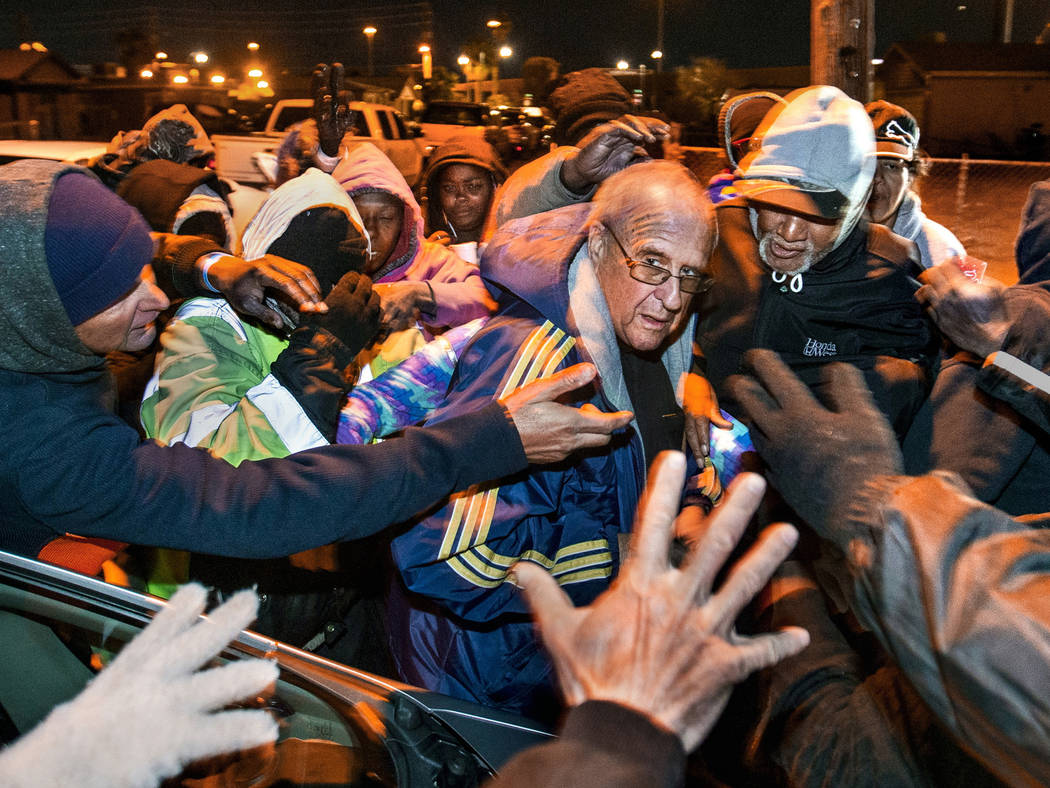 A crowd gathers around Father John McShane as he gives away bus passes and other supplies durin ...