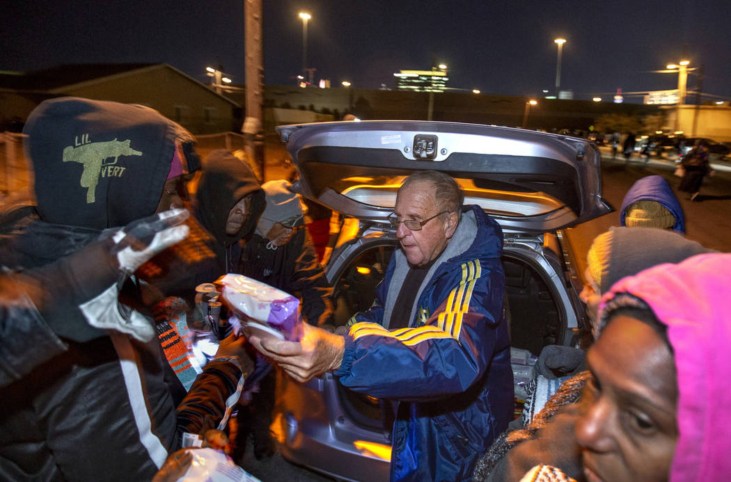 Father John McShane, center, passes out baby wipes and blankets to those in need gathered about ...