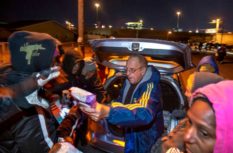 Father John McShane, center, passes out baby wipes and blankets to those in need gathered about ...