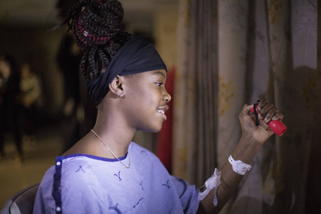 Zion Green, 12, shines a flashlight back at a crowd of people in the parking lot flashing light ...