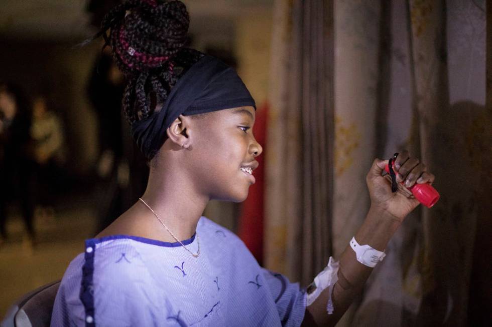 Zion Green, 12, shines a flashlight back at a crowd of people in the parking lot flashing light ...