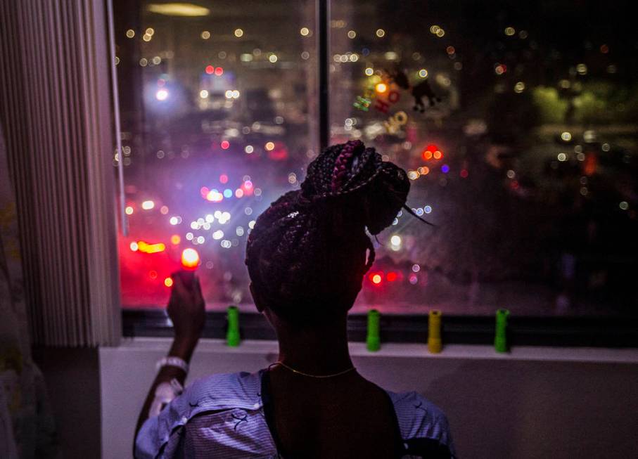 Zion Green, 12, shines a flashlight back at a crowd of people in the parking lot flashing light ...