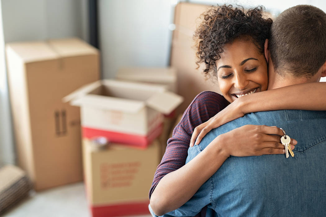 Young african woman holding home keys while hugging boyfriend in their new apartment after buyi ...