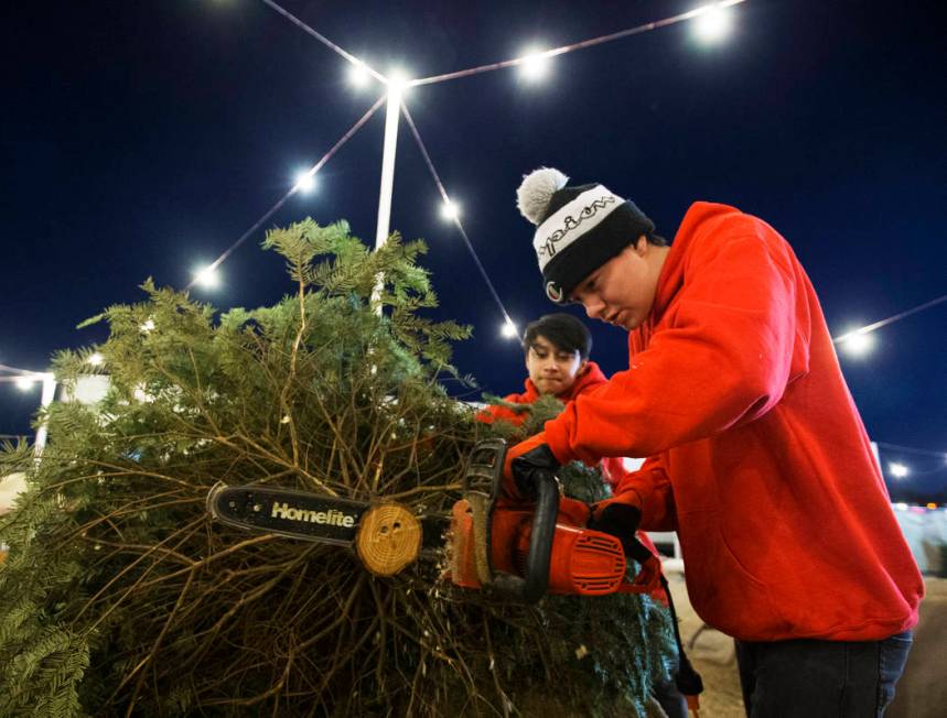 Phoenix Dante, right, and Lincoln Shorter make a fresh cut to the trunk of a Christmas tree on ...