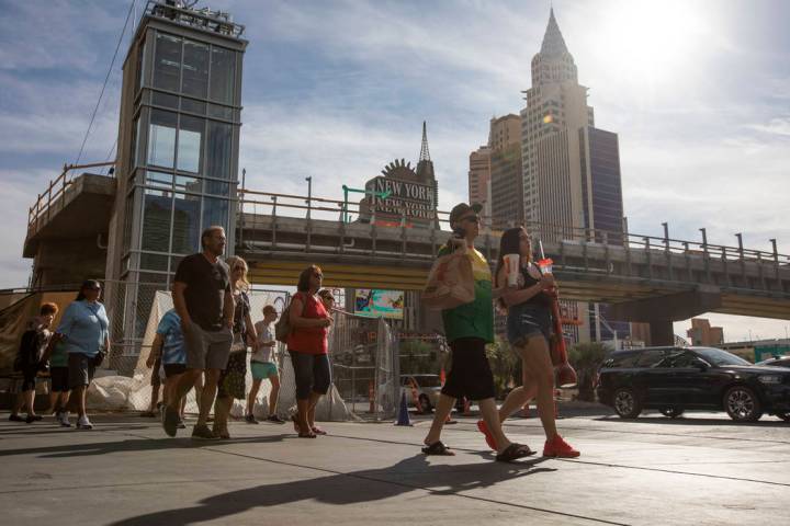 People walk along Las Vegas Boulevard in front of the pedestrian bridge being constructed to im ...