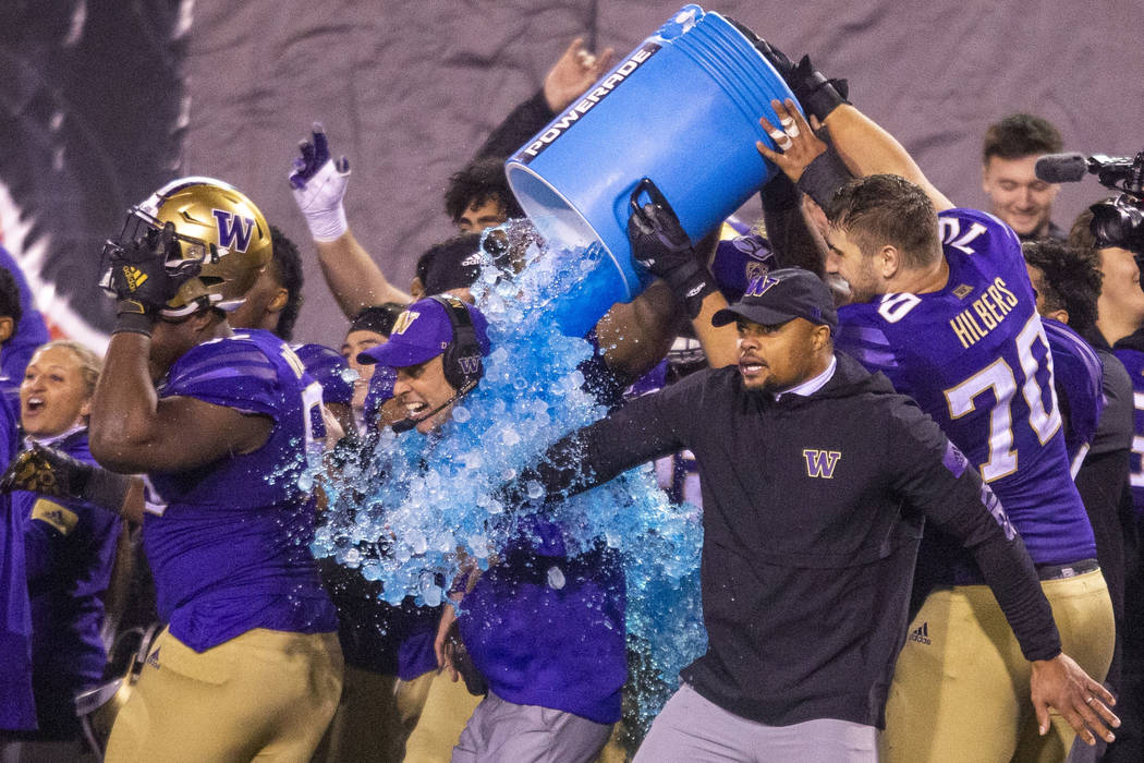Washington Huskies head coach Chris Petersen, center, is soaked with Powerade and ice ending th ...