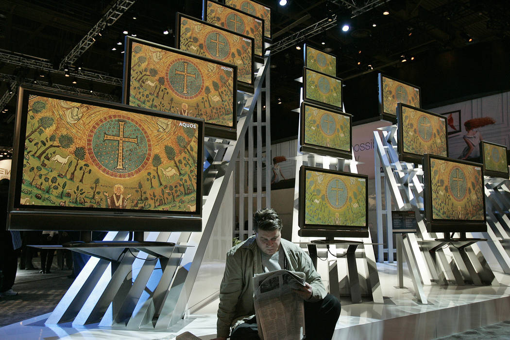A man reads the paper by a display of digital cable ready televisions at the 2005 Consumer Elec ...