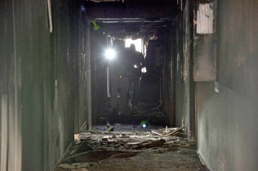 Investigators walk through an interior corridor after a fire at a three-story apartment complex ...