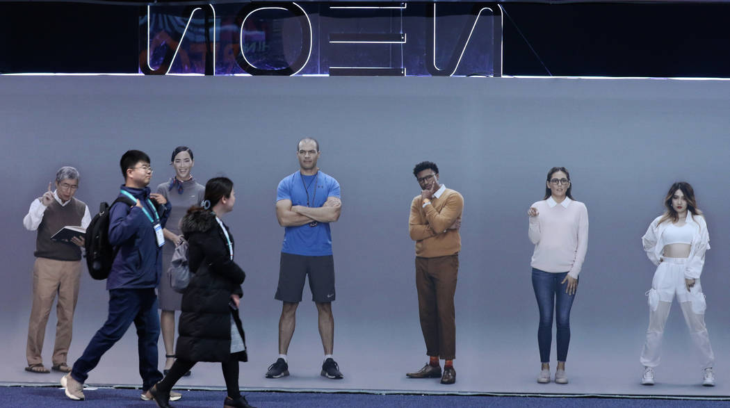 Conventiongoers walk pass Neon's, a computationally created virtual being that looks and behave ...