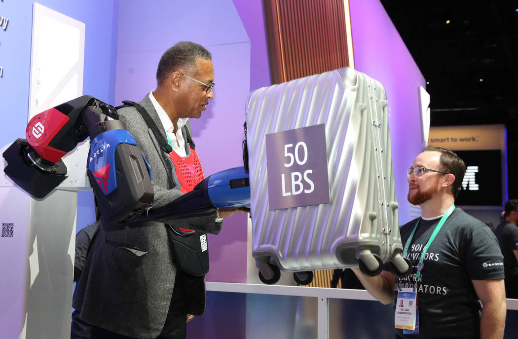 Bill Easter, left, of Delta Airlines, Inc., using upper-body exoskeleton, lifts a 50 lb suitcas ...
