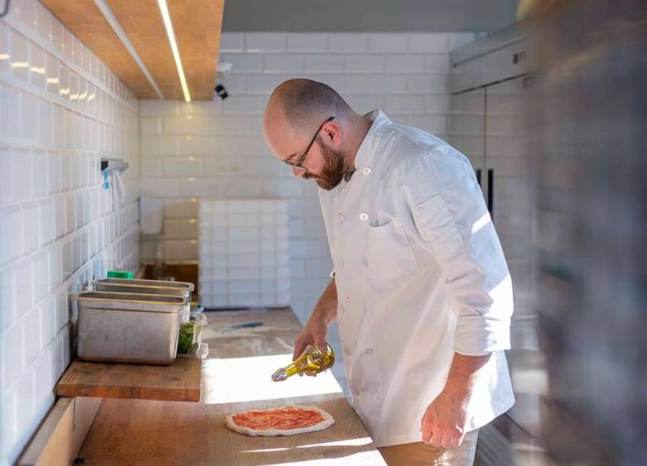 Chef Bartosz Wawrzyszak, owner of the Custom Pizza Truck, drizzles olive oil onto dough while m ...