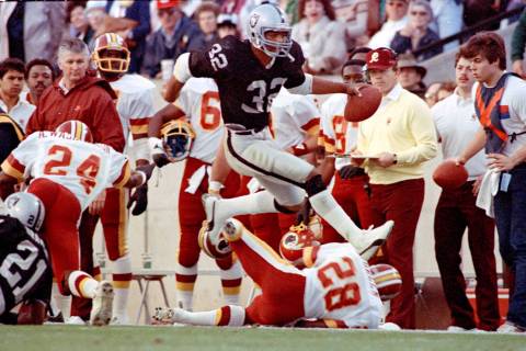 Los Angeles Raiders running back #32 Marcus Allen high steps his way down the sideline past Was ...