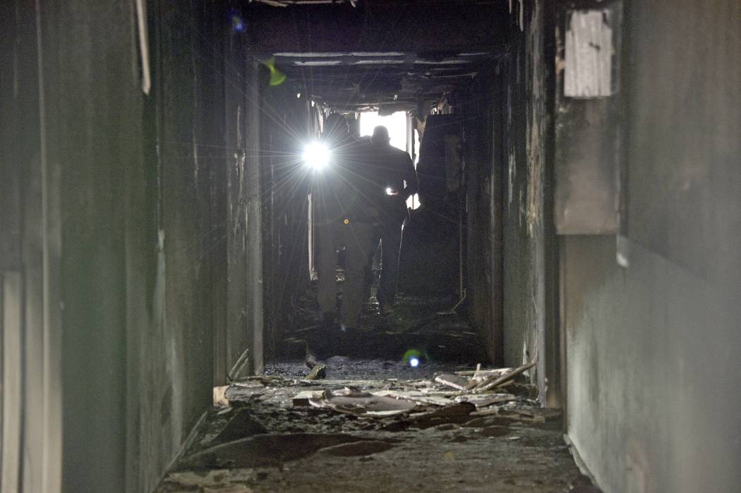 Investigators walk through an interior corridor after a fire at a three-story apartment complex ...