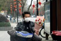 A man wearing a face mask carries a Valentine's Day bouquet as he rides a scooter in Hangzhou i ...