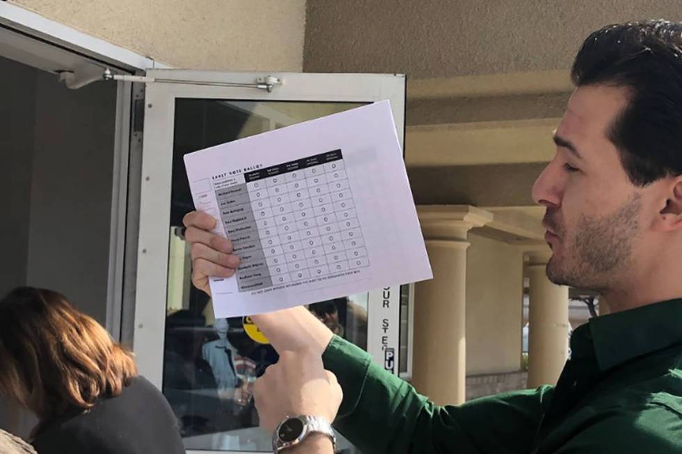 A poll worker explains the paper ballot with those waiting in line at 3511 E. Harmon Ave. on Su ...