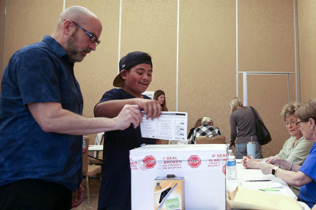 Preston Ribeiro-Salavea, 10, of Henderson helps his father Scott Ribeiro, 56, drop his ballot d ...