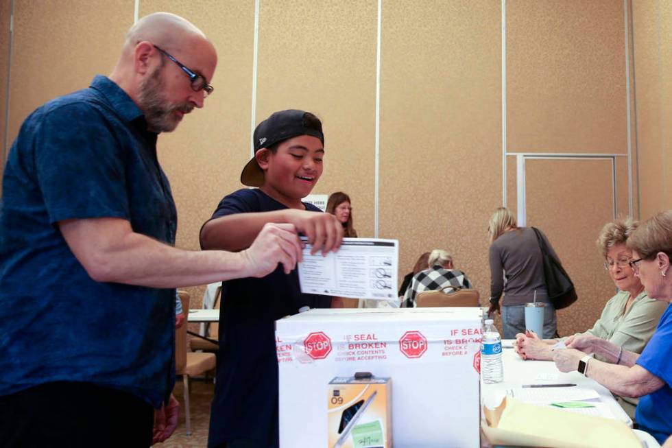 Preston Ribeiro-Salavea, 10, of Henderson helps his father Scott Ribeiro, 56, drop his ballot d ...