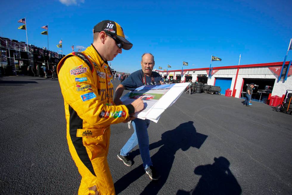Kyle Busch signs an autograph for a fan as he walks back to the garage area during practice for ...