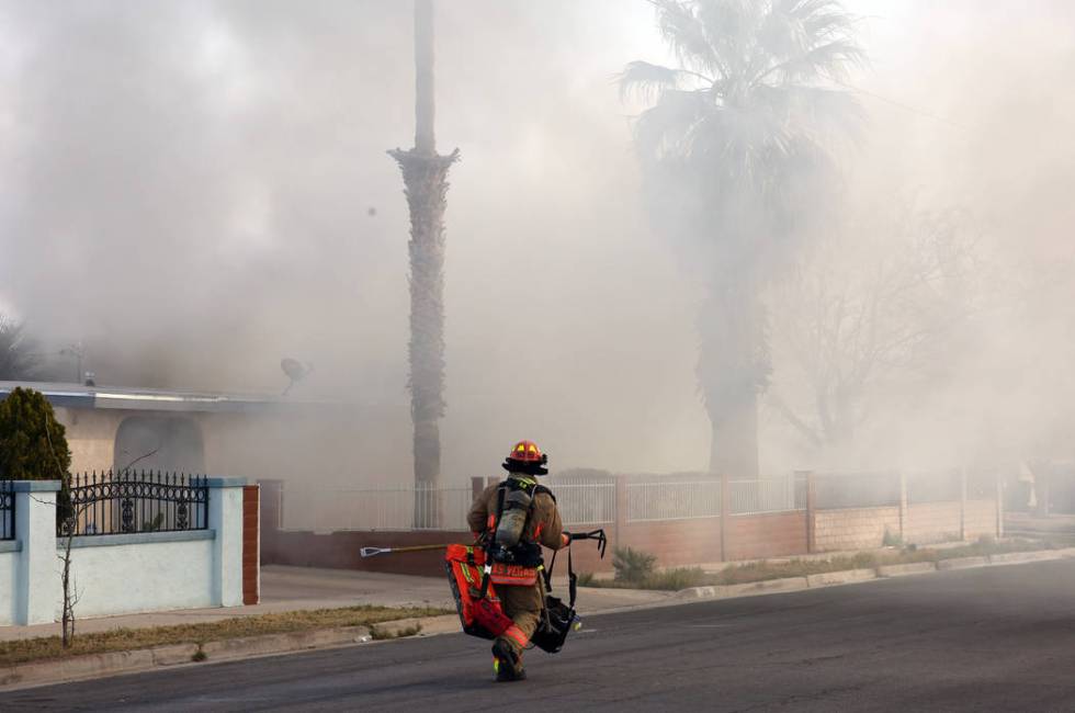 Heavy smoke is seen as a Las Vegas firefighter prepares to battle a house fire at 2417 Howard D ...