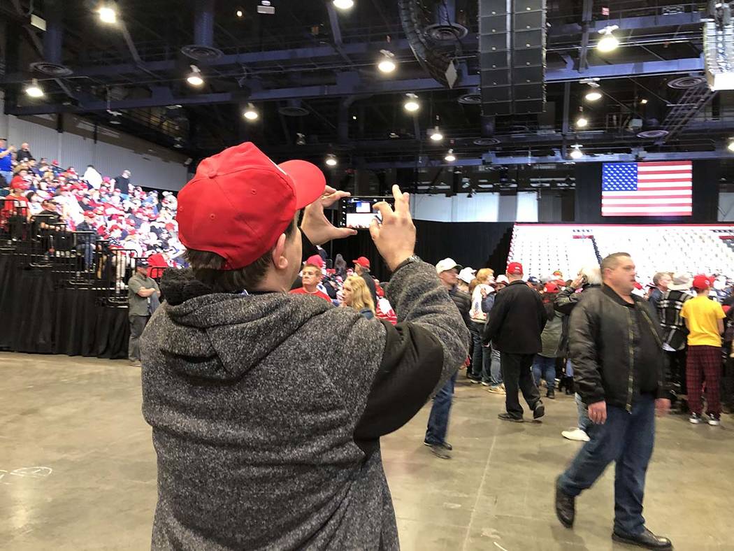 A man positions his phone to catch the full crowd pressed up against the fence around the podiu ...