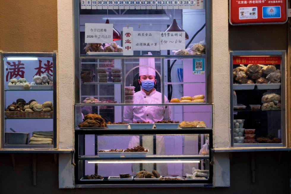 a chef looks out from behind a display of food products at a restaurant in Beijing, China, Satu ...