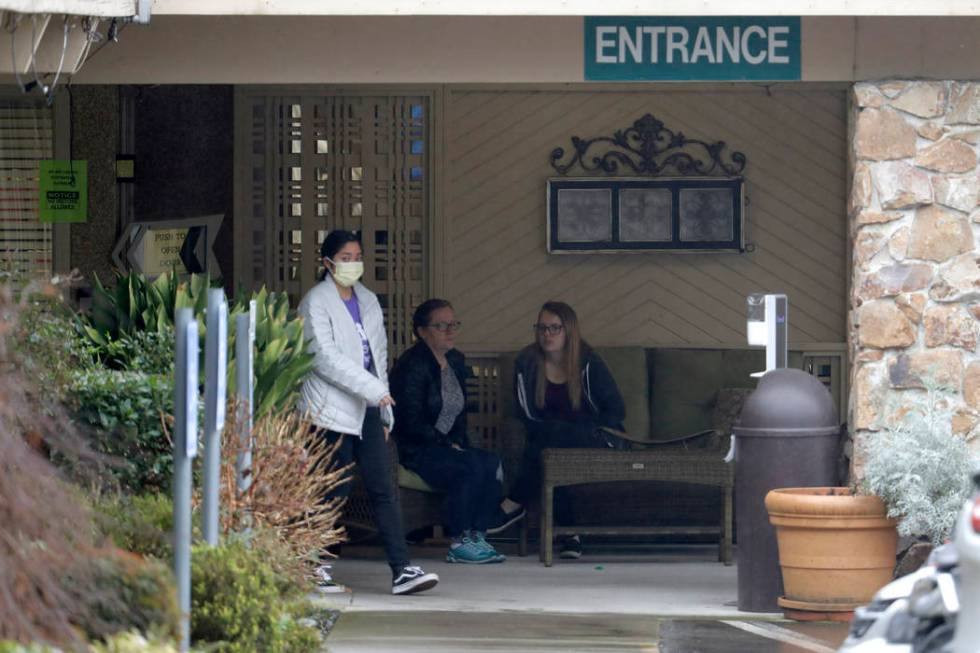 A person wearing a mask walks past a sign banning visitors at the Life Care Center in Kirkland, ...