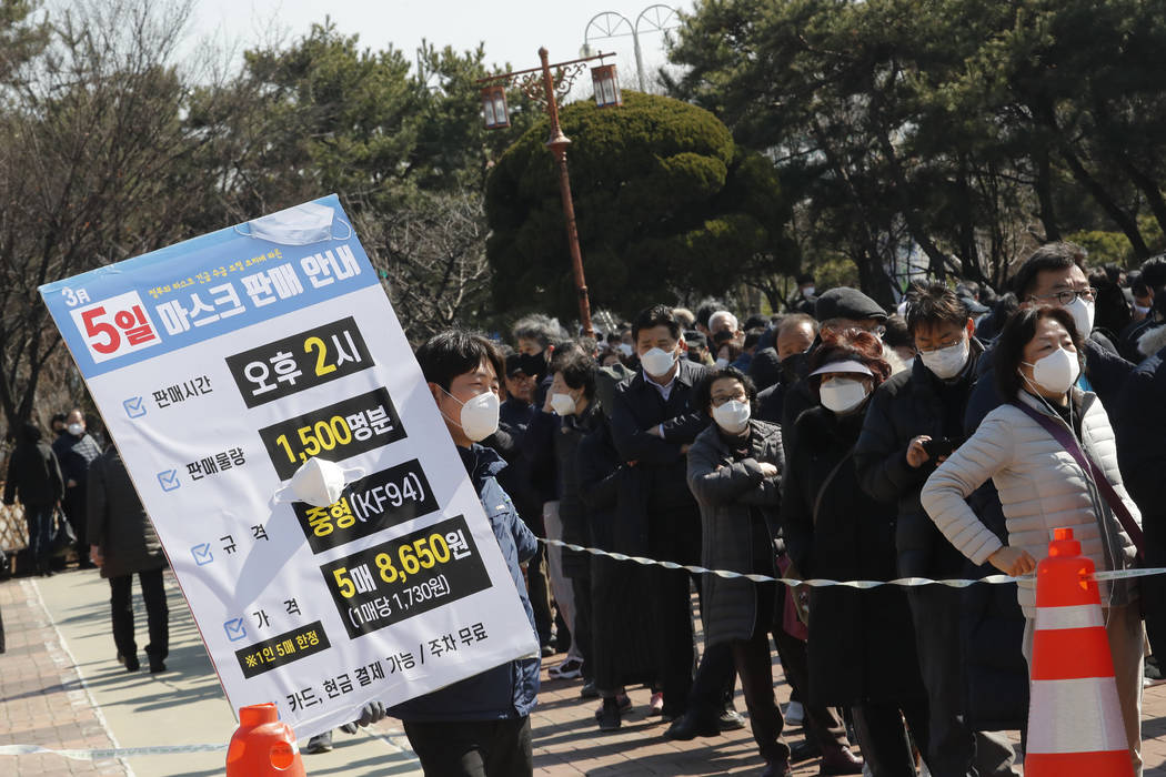 An employee holds a board to give face mask sales informations as people line up to buy face ma ...