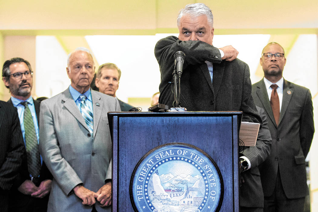 Governor Steve Sisolak demonstrates the best way to cough without spreading disease during a pr ...
