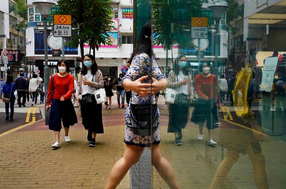 People wearing face masks walk at a street in Hong Kong Friday, March. 13, 2020. For most, the ...