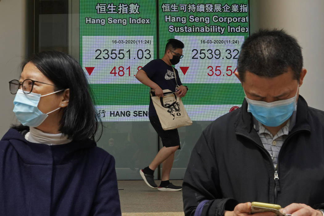 People wearing face masks walk past a bank electronic board showing the Hong Kong share index a ...