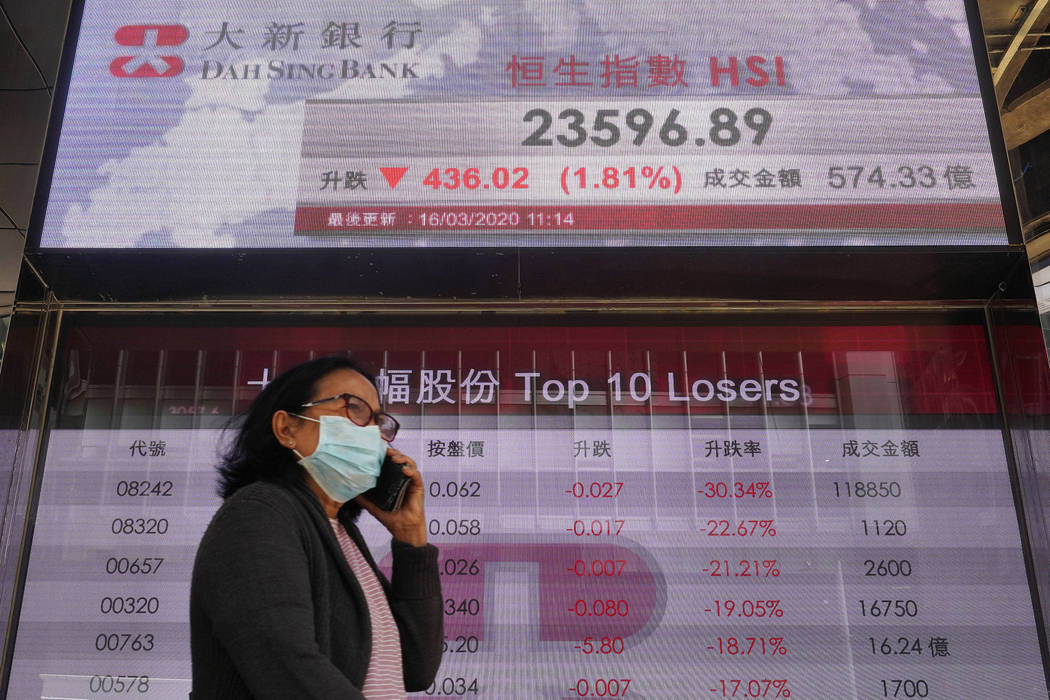 A woman wearing face mask walks past a bank electronic board showing the Hong Kong share index ...