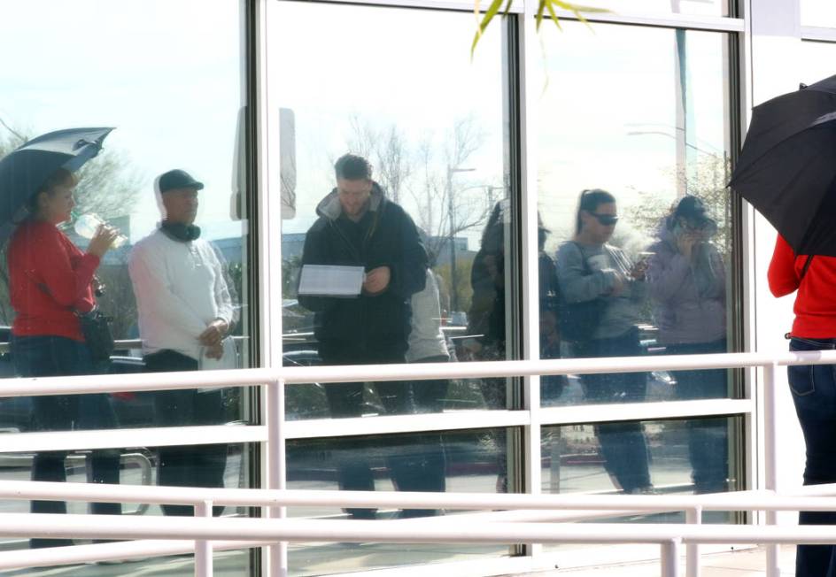 People are reflected on glass windows as they wait in line at One-Stop Career Center on Monday, ...